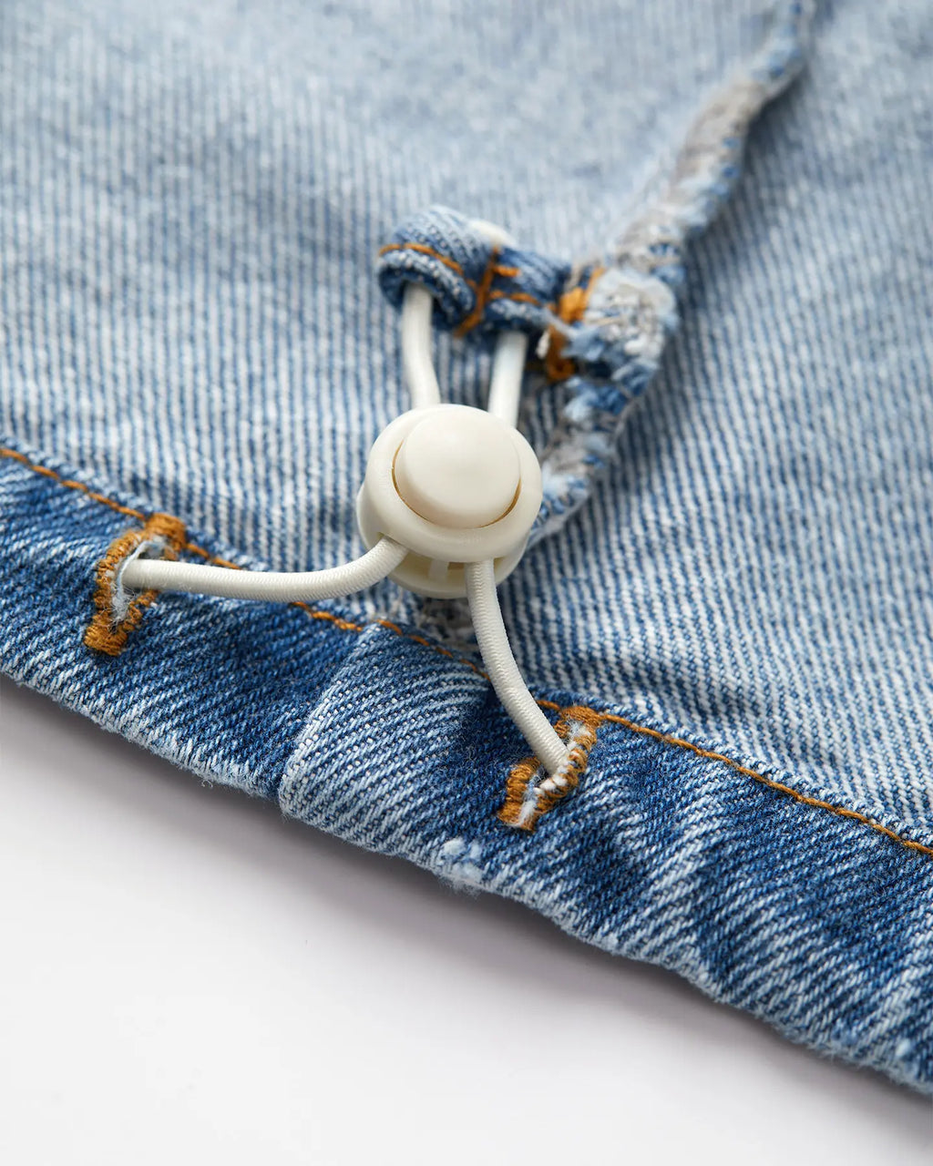 Detalle de jeans en denim color azul piedra desteñido con pespuntes en naranja, confeccionados en algodón, presenta un acabado con cordón elástico ajustable para mayor comodidad.