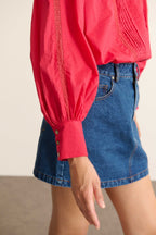 Frau in der Bluse BELLA in der Farbe Kirsche, eine weite Bluse aus Baumwollvoile mit Spitzeneinsatz und Falten.