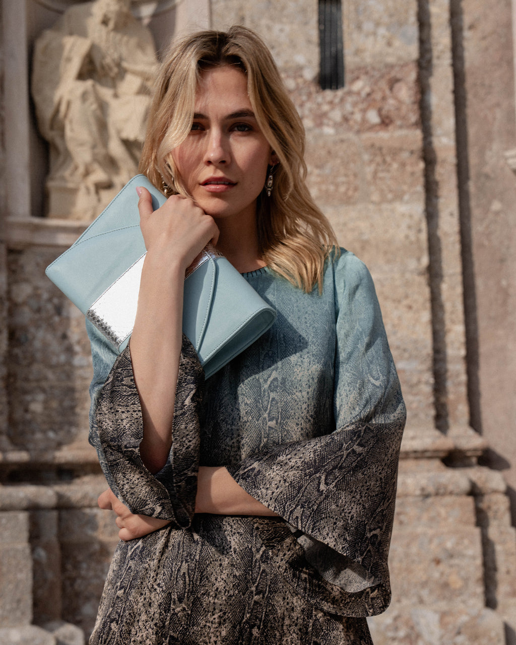 Michonet – Robe Aqua Snake, mannequin femme blonde en robe imprimée, tenant une pochette bleue