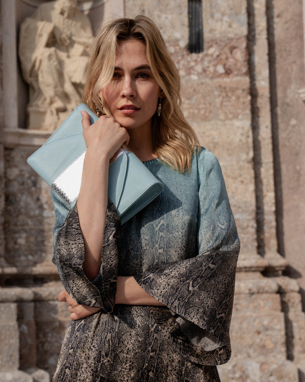 Michonet – Robe Aqua Snake, mannequin femme blonde en robe imprimée, tenant une pochette bleue