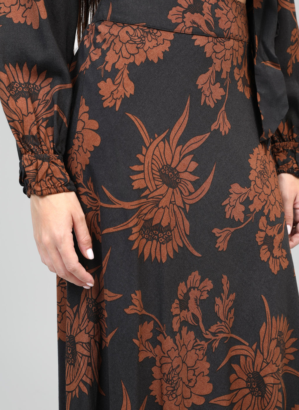 An'ge – Jupe Midi Gania Floflo Caramel, mannequin portant une robe noire à motifs floraux marron, vue de côté