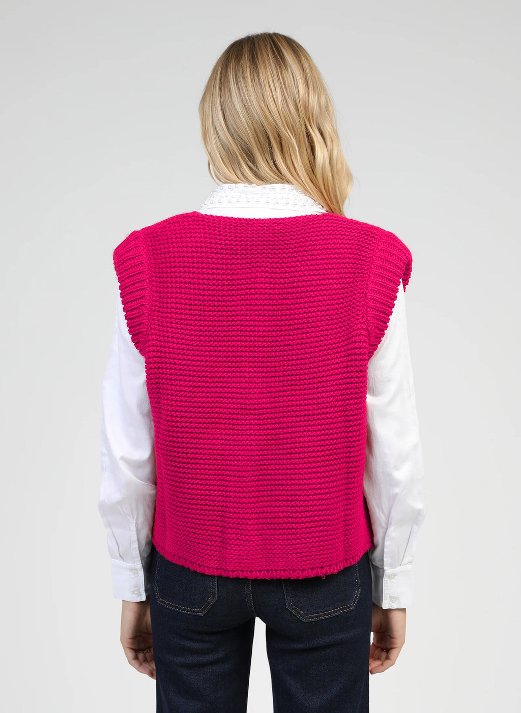 An'ge – Gilet Legringo Fushia, model van achteren gekleed in een fuchsiazwevend gebreid vest over een witte blouse