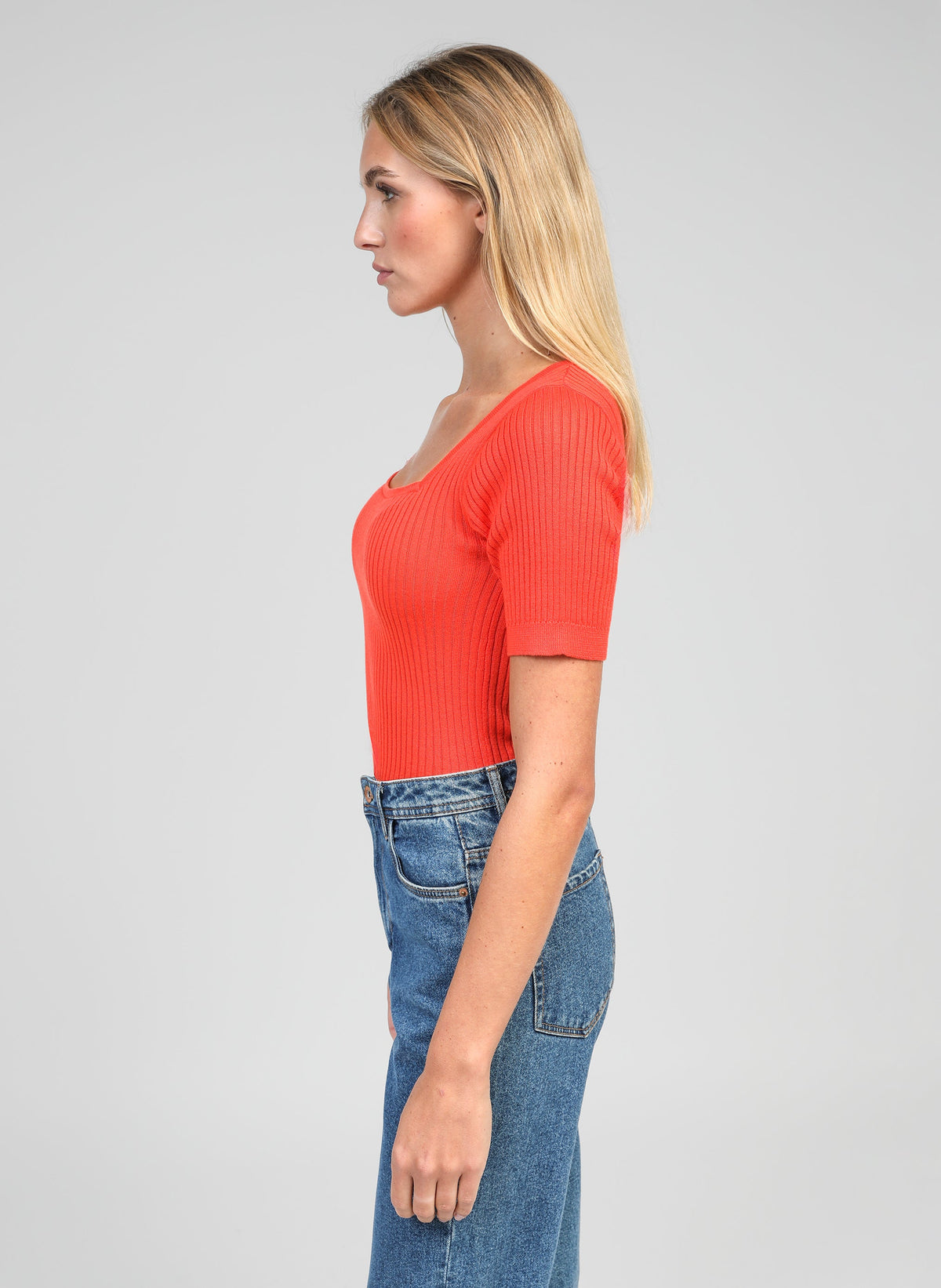 An'ge – Pull Lesia Piment, mannequin portant un haut côtelé rouge et un jean bleu, vue de profil