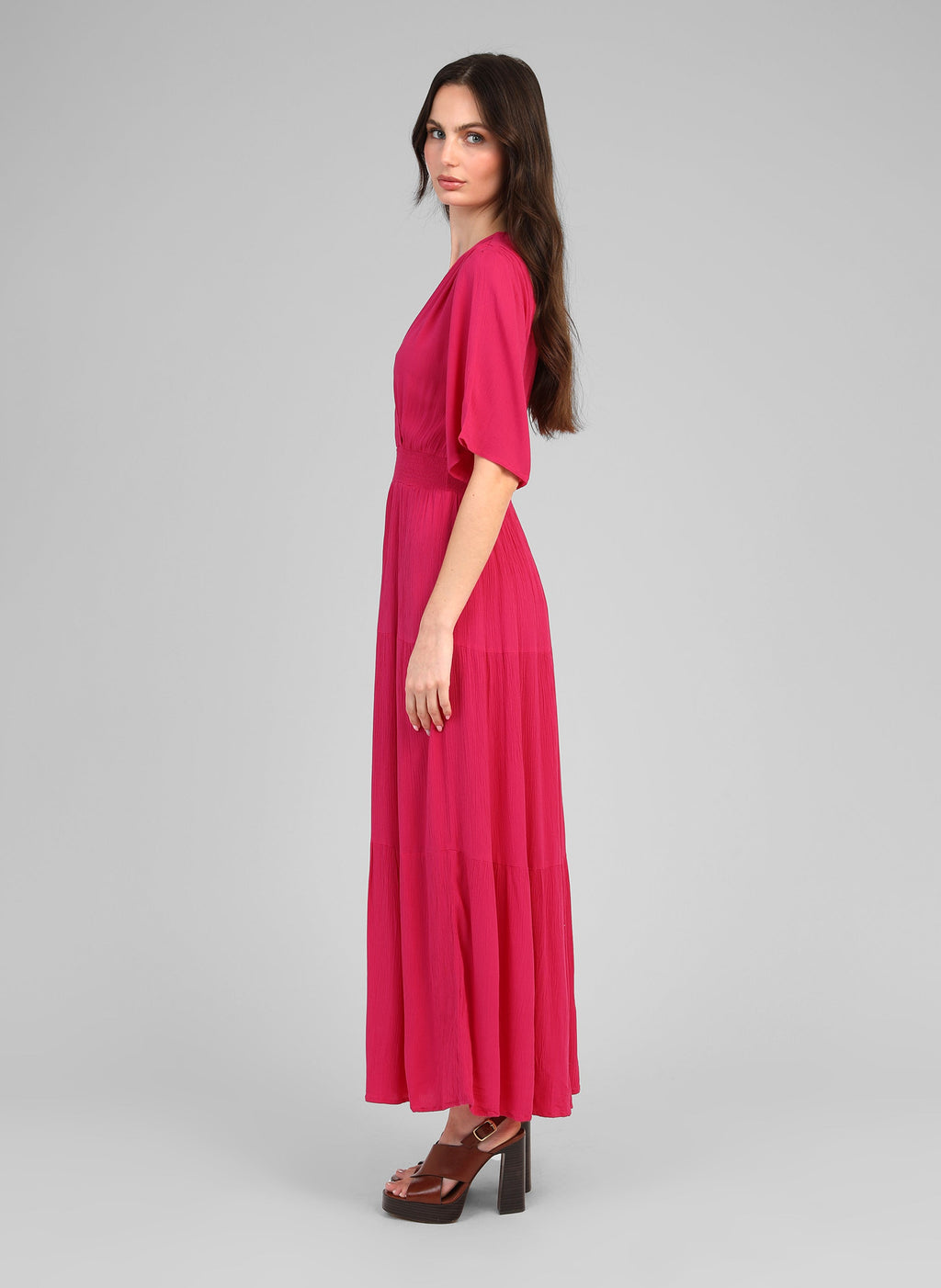 An'ge – Langes Kleid Osunchala Fuchsia, Model im Profil im langen fließenden fuchsiafarbenen Kleid und Sandalen