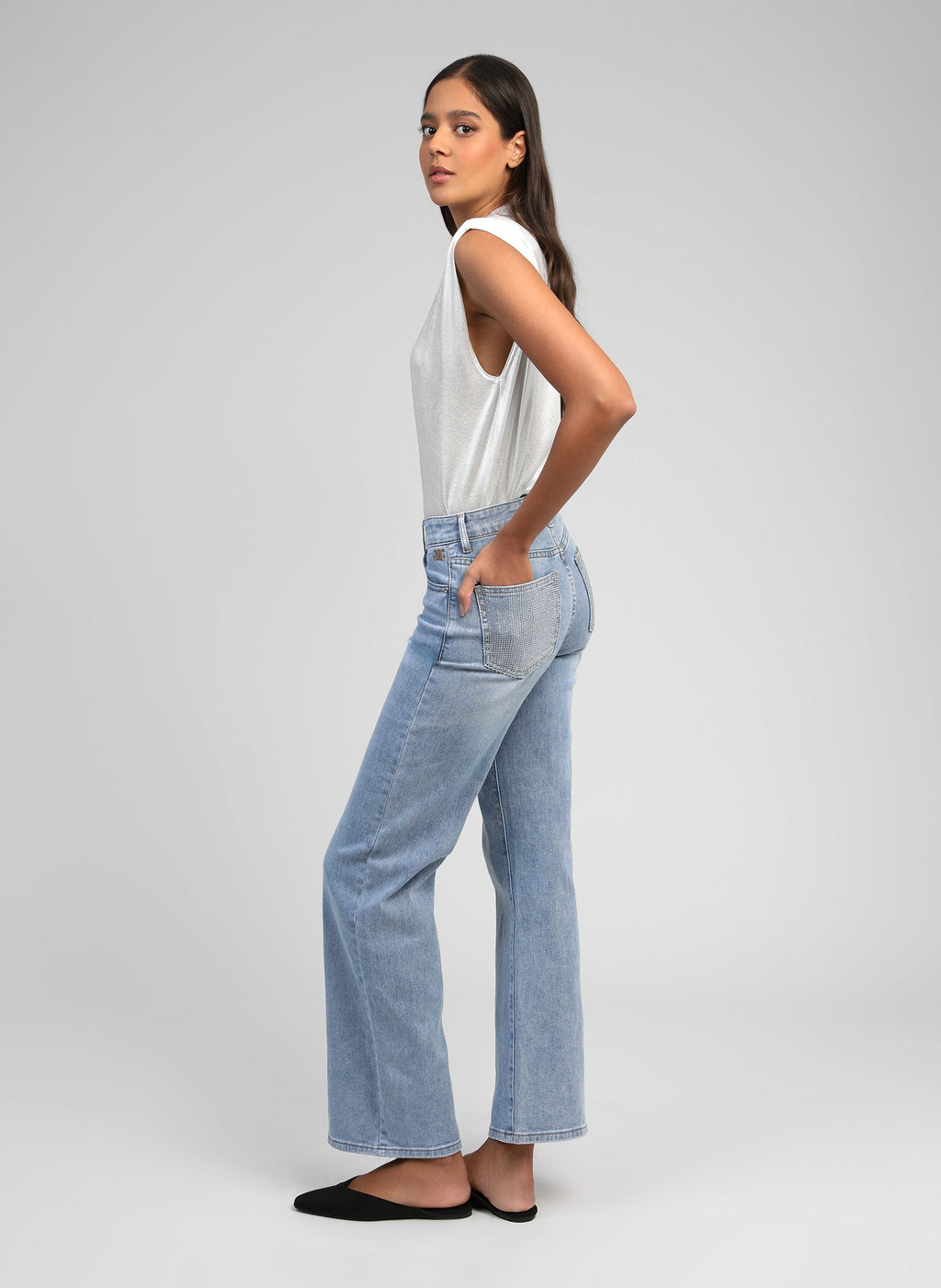 An'ge – Pantalon Pipoche Bleu Ciel, modelka z profilu ubrana w biały top na ramiączkach i jasnoniebieskie jeansy