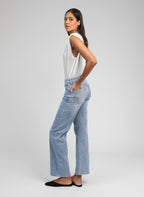 An'ge – Pantalon Pipoche Bleu Ciel, modelka z profilu ubrana w biały top na ramiączkach i jasnoniebieskie jeansy