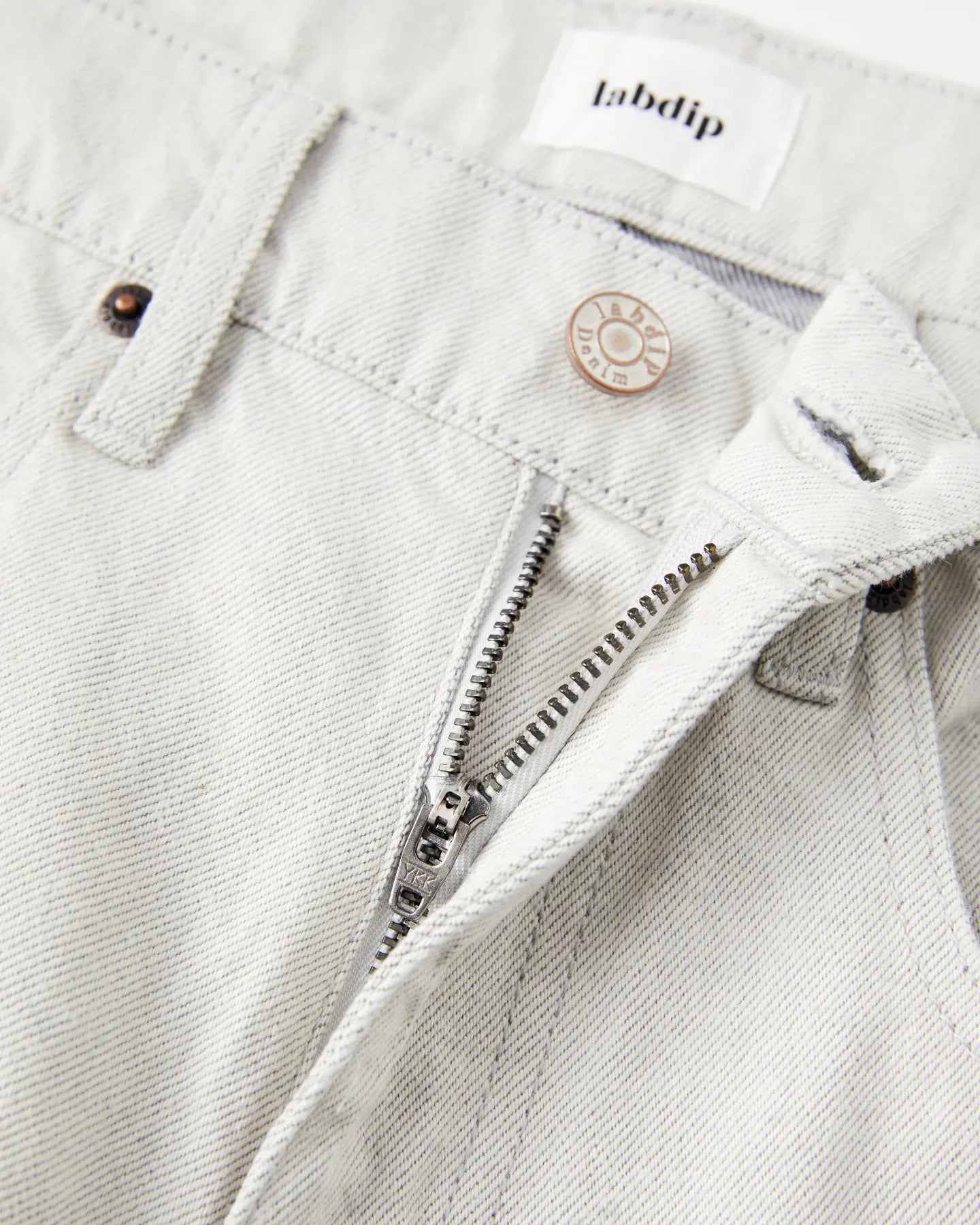 Jean pour femme en denim non teinté couleur granit clair, coupe droite avec fermeture éclair et bouton métal gravé, confection 100% coton avec finition sobre et naturelle.