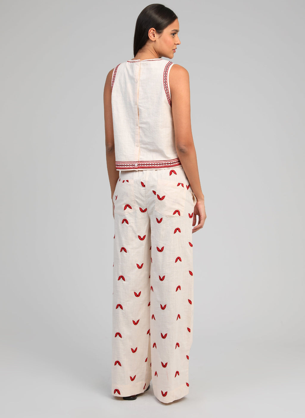 An'ge – Pantalon Romila Ecru, model van achteren draagt een gebroken witte set geborduurd met rode motieven
