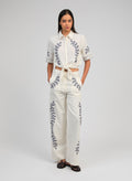 An'ge – Pantalon Rossalie Ecru, mannequin portant un ensemble blanc brodé de motifs végétaux bleus, vue de face
