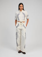 An'ge – Pantalon Rossalie Ecru, mannequin portant un ensemble blanc brodé de motifs végétaux bleus, vue de face