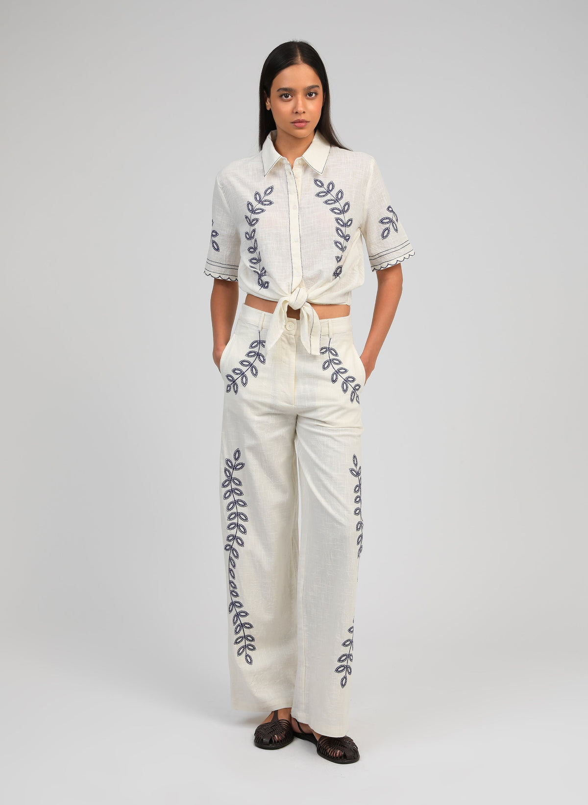 An'ge – Pantalon Rossalie Ecru, mannequin portant un ensemble blanc brodé de motifs végétaux bleus, vue de face