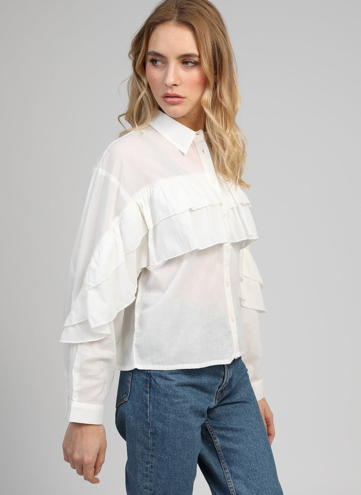 An'ge – Camicia Suprema Blanc, modella che indossa una camicia bianca con volant e jeans blu