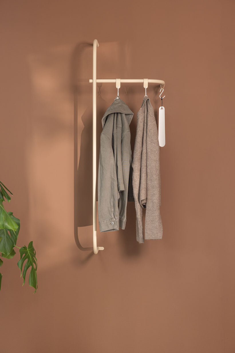 Garderobe TAMINA mit minimalistischer Metallstange und hängenden Kleidungsstücken an einer braunen Wand.