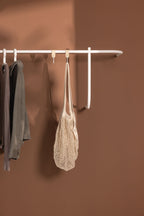 Garderobe TAMINA mit minimalistischen Metallstangen und Kleidungsstücken an der Wand.