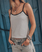 Woman wearing a striped tank top and jeans against a blue wall.