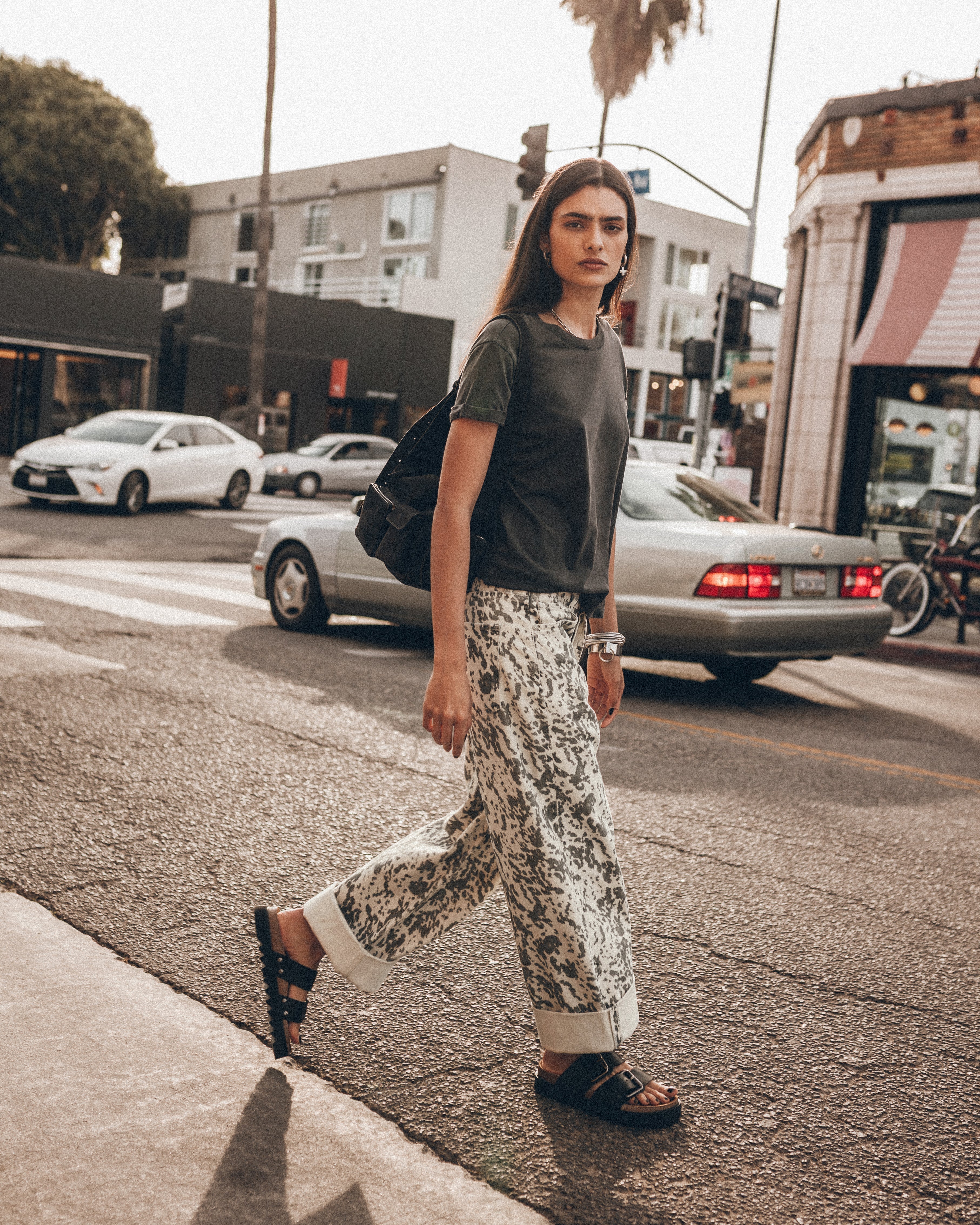 Persona caminando por una calle de la ciudad con una camisa verde y pantalones estampados.