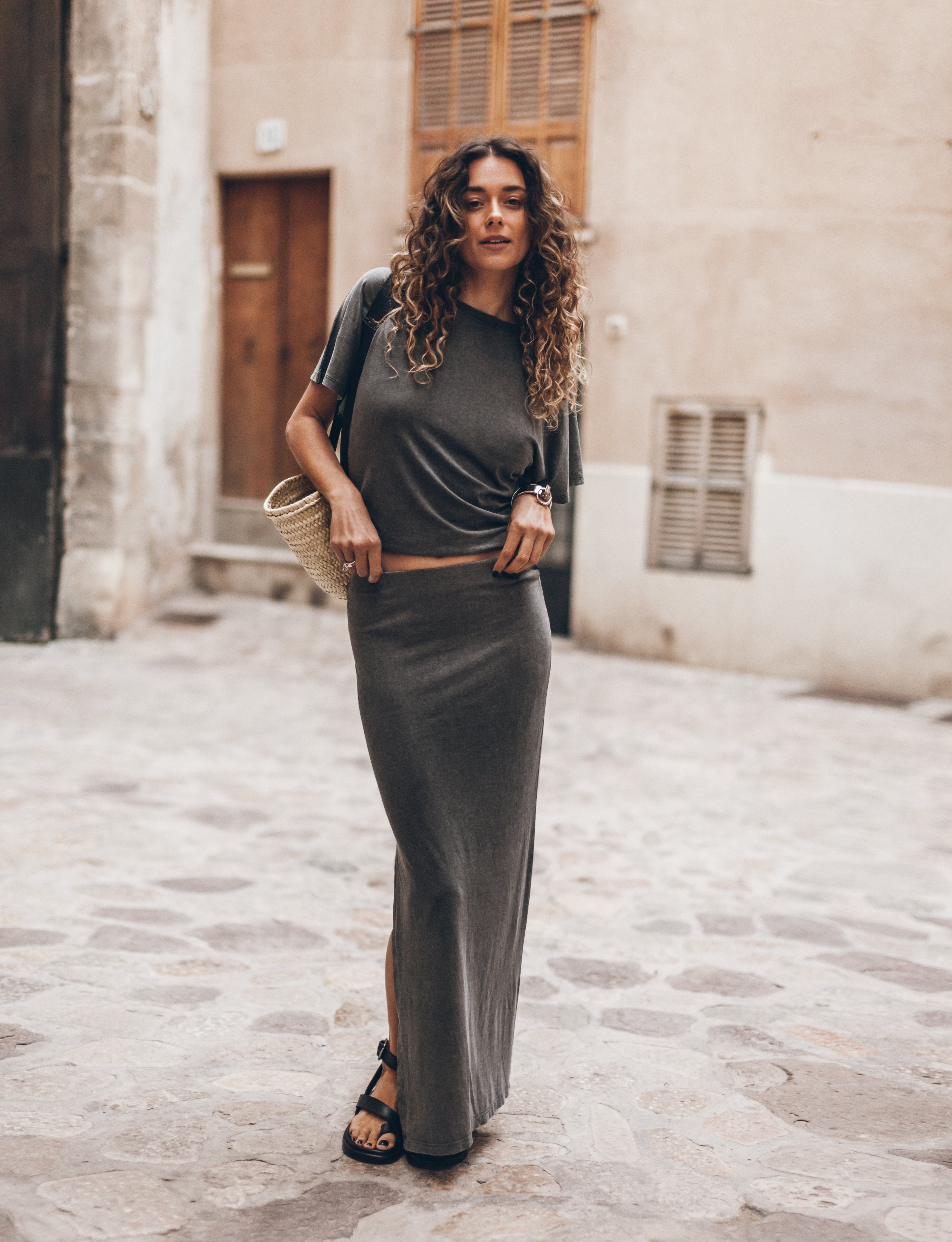 Woman in a gray outfit standing on a stone street with buildings in the background