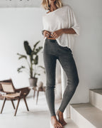 Person wearing a white oversized shirt and gray leggings standing on a staircase in a bright room with plants.