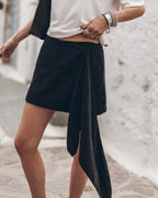 Mujer vestida con una falda cruzada negra y una camiseta blanca sobre un fondo claro.