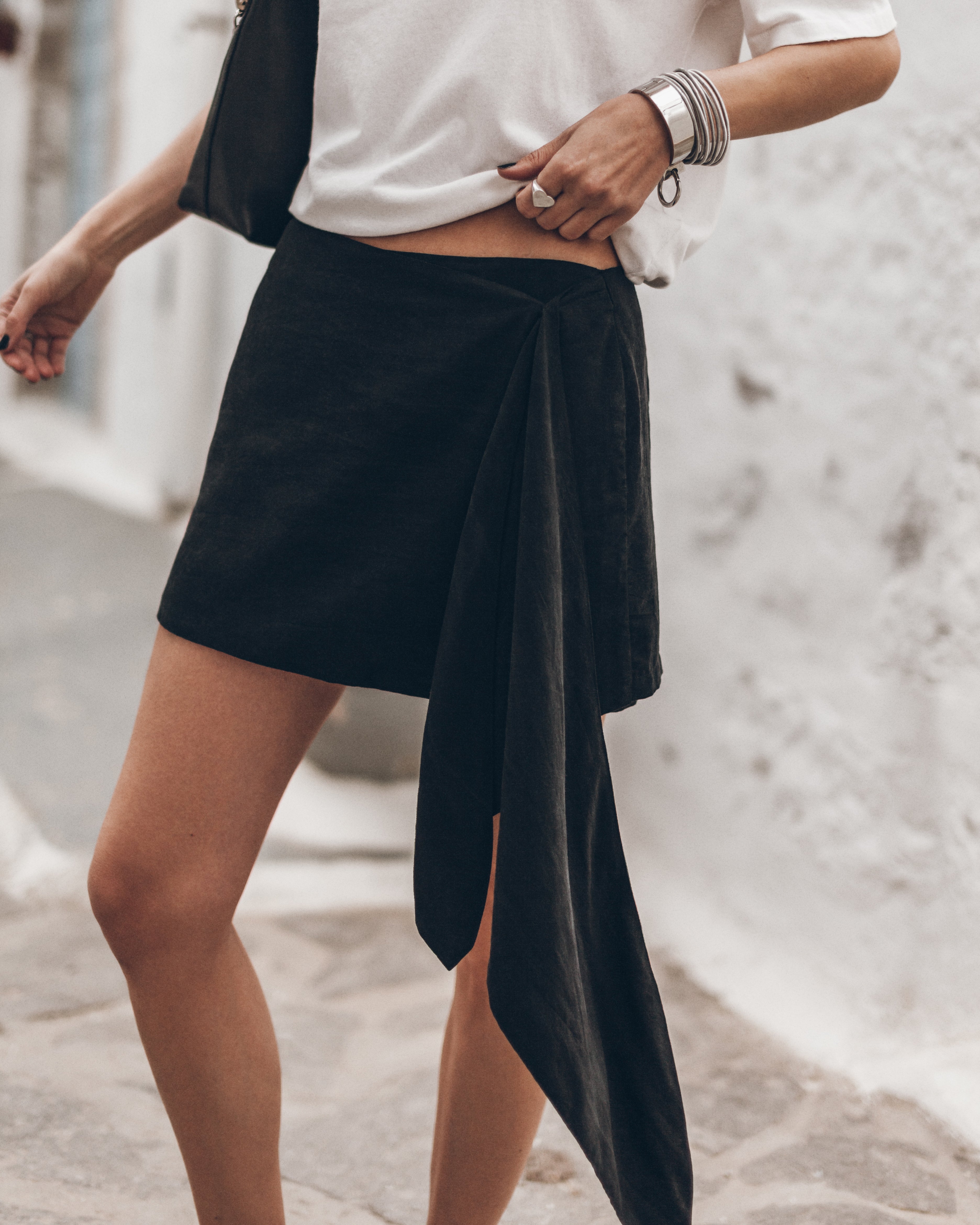 Mujer vestida con una falda cruzada negra y una camiseta blanca sobre un fondo claro.